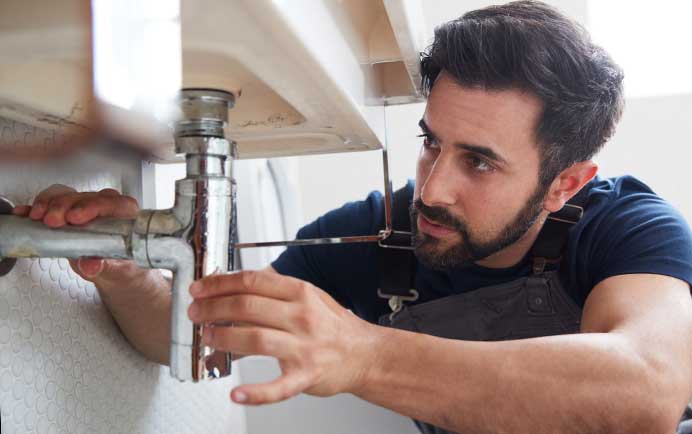 Plumber repairing a drain pipe beneath a bathroom sink